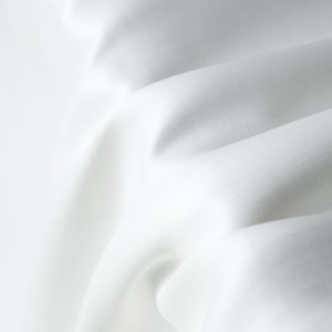 Puede incluir: Primer plano de tela blanca con pliegues suaves y sombras sutiles. La tela parece lisa y fluida, con un ligero brillo. La imagen resalta la textura y la ca&iacute;da del material, sugiriendo un textil lujoso.