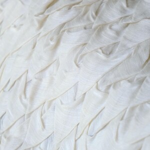 May include: Close-up of a white fabric with a textured, layered design. The fabric appears to be soft and has a rippled effect, creating a pattern of folds and ridges. The color is a bright, clean white.