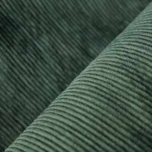 May include: Close-up of a textured, dark green corduroy fabric. The fabric has a ribbed pattern running diagonally across the image, creating a sense of depth and texture. The corduroy appears soft and plush, with a slight sheen.