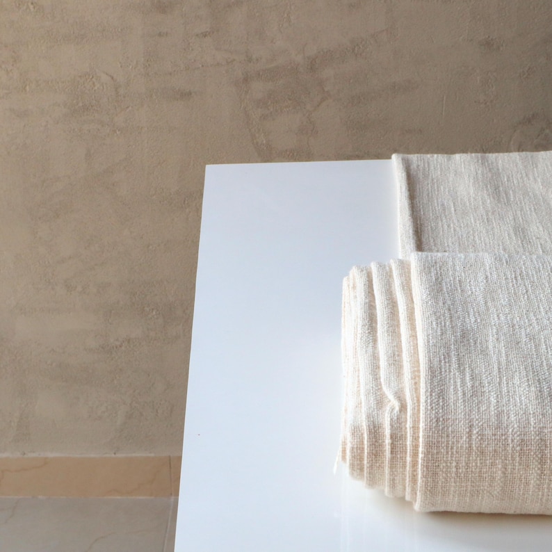 May include: A white, rolled up fabric on a white surface. The fabric has a subtle texture and is folded neatly.