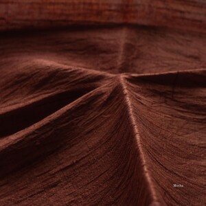 May include: Close-up of a textured fabric in a rich mocha brown color. The fabric has visible woven lines and folds, creating a sense of depth and texture. The word "Mocha" is visible in the bottom right corner.