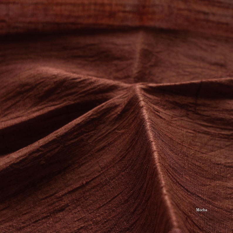 May include: Close-up of a textured fabric in a rich mocha brown color. The fabric has visible woven lines and folds, creating a sense of depth and texture. The word "Mocha" is visible in the bottom right corner.