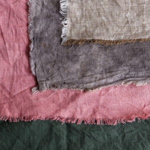 May include: Three fabric swatches with frayed edges. The top swatch is a light beige, the middle swatch is a dark grey, and the bottom swatch is a light pink.