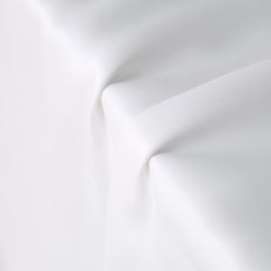 Puede incluir: Primer plano de tela blanca con pliegues y sombras suaves. La tela parece lisa y opaca, con una textura sutil. La iluminaci&oacute;n crea reflejos y sombras, enfatizando las curvas y la profundidad del material.