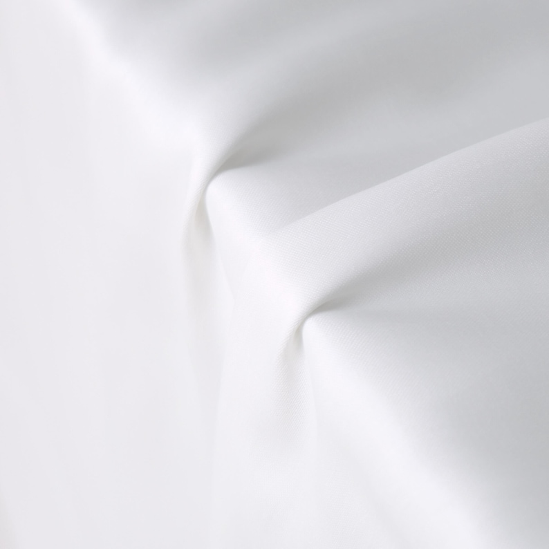 Puede incluir: Primer plano de tela blanca con pliegues y sombras suaves. La tela parece lisa y opaca, con una textura sutil. La iluminaci&oacute;n crea reflejos y sombras, enfatizando las curvas y la profundidad del material.