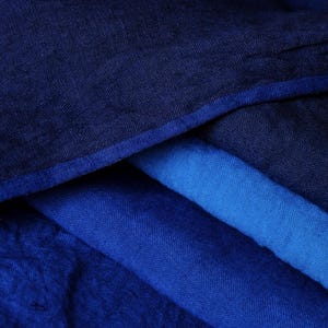 Può includere: Primo piano di tessuto blu piegato in varie tonalità. L'immagine mostra una gamma di blu, dal blu navy scuro a una tonalità più chiara e brillante. Il tessuto appare morbido e strutturato, con dettagli di trama visibili.