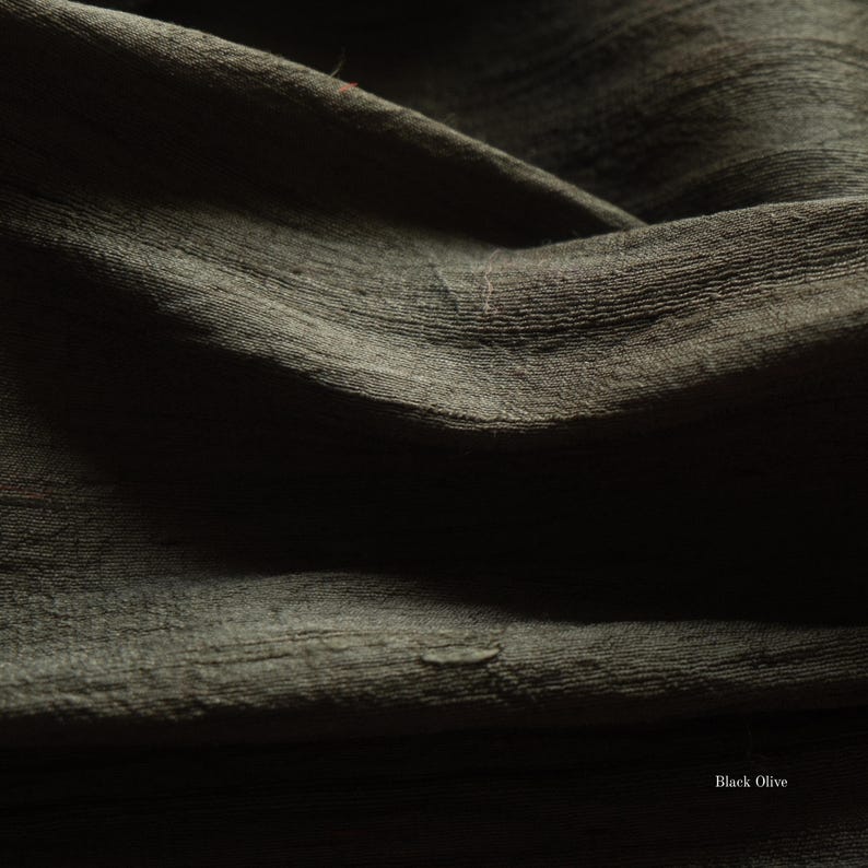 May include: Close-up of a dark olive green fabric with a textured, slightly wrinkled surface. The fabric has a subtle sheen and appears to be draped, with visible folds and shadows. The words "Black Olive" are in the bottom right corner.