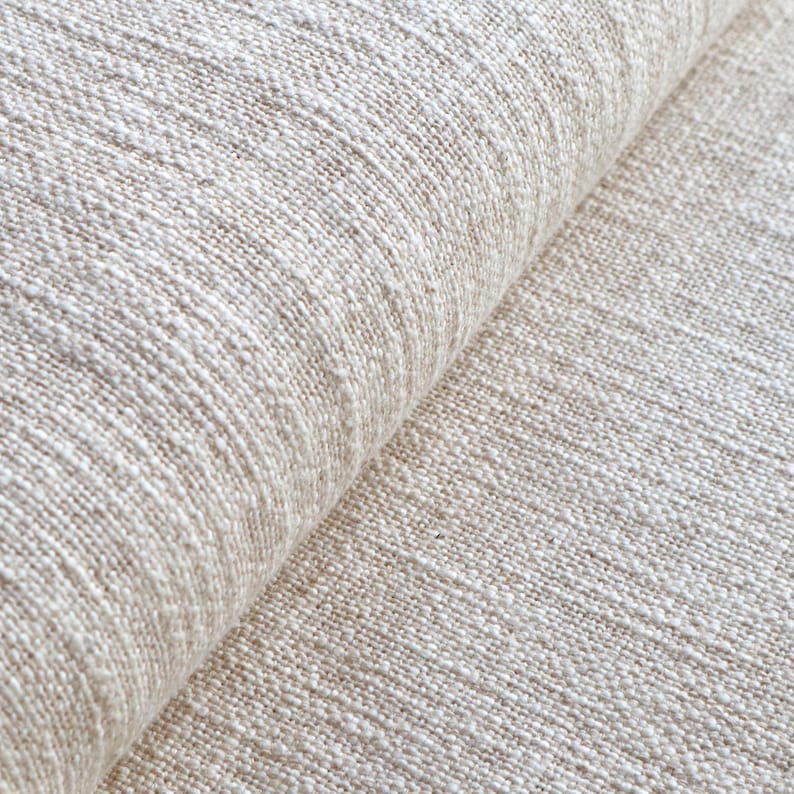 May include: Close-up of a beige fabric with a textured weave. The fabric is folded in half, showing the texture on both sides.