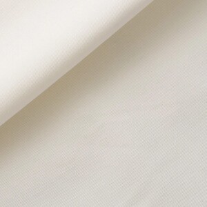 K&ouml;nnte beinhalten: Eine Nahaufnahme von einfarbigem wei&szlig;em Stoff mit einem ausgepr&auml;gten diagonalen K&ouml;perbindungsmuster. Das Material ist an der oberen linken Ecke umgeschlagen und zeigt die Textur und die gleichm&auml;&szlig;ige cremewei&szlig;e Farbe der Textiloberfl&auml;che.