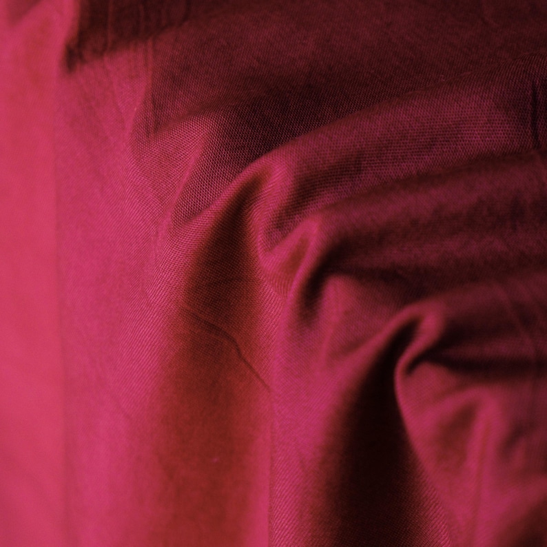 Pode incluir: Close-up de um tecido magenta profundo com textura e dobras vis&iacute;veis. O tecido tem um leve brilho e a ilumina&ccedil;&atilde;o cria sombras que real&ccedil;am a textura. O efeito geral &eacute; rico e luxuoso.