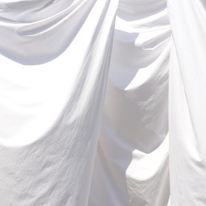 May include: White fabric sheets hanging on a clothesline, creating soft folds and shadows. The fabric is smooth and appears to be freshly laundered.