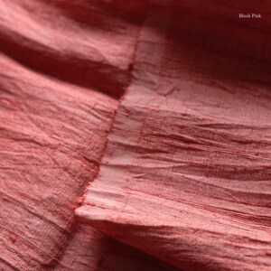 May include: Close-up of blush pink fabric with a textured, wrinkled appearance. The fabric has a raw edge and visible horizontal lines. The words "Blush Pink" are in the upper right corner.