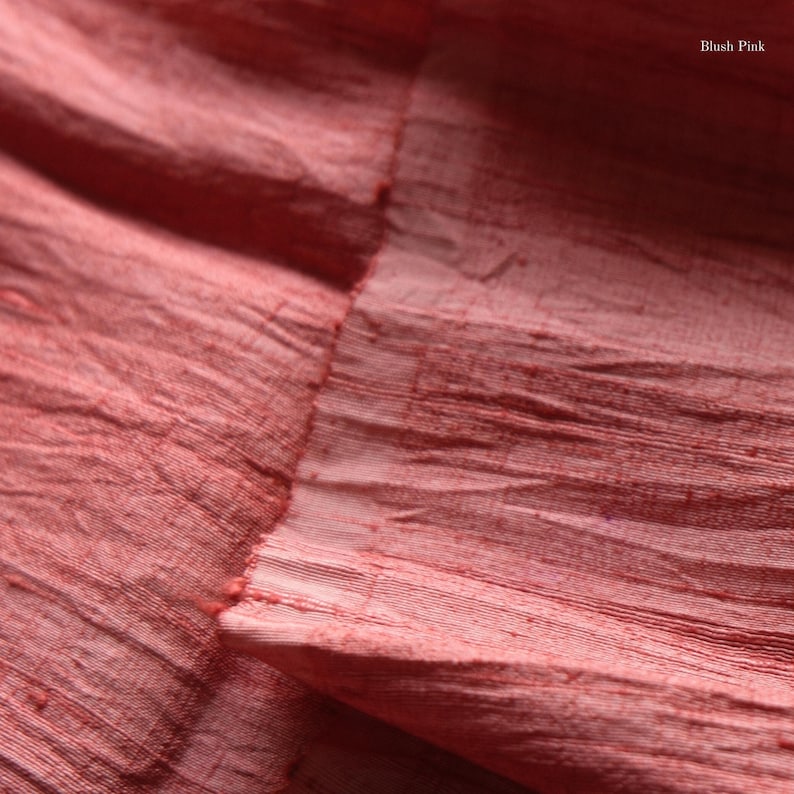 May include: Close-up of blush pink fabric with a textured, wrinkled appearance. The fabric has a raw edge and visible horizontal lines. The words "Blush Pink" are in the upper right corner.