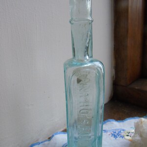 May include: A clear glass bottle with a square body and a narrow neck. The bottle has a textured surface and the word "HOSTETTER'S" is visible on the front.