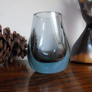 May include: A small, clear glass vase with a blue tint and a rounded bottom. The vase is sitting on a wooden surface.