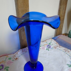 A very tactile lily vase in cobalt blue glass. An elegant design, round base ,conical body and wavy rim. Stands well, would grace any home.