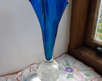 Könnte beinhalten: Eine blaue Glasvase mit einem gekräuselten oberen Rand und einem klaren Glasfuß mit einem strukturierten Blasendesign.
