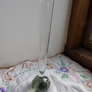 May include: A clear glass bud vase with a textured, grey, bubbled base.