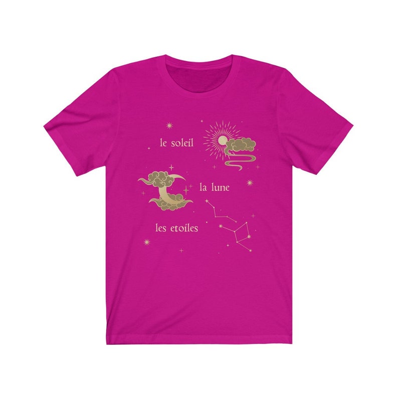 Puede incluir: Una camiseta rosa fucsia con un dise&ntilde;o gr&aacute;fico dorado de un sol, una luna y estrellas. El texto "le soleil", "la lune" y "les etoiles" est&aacute; impreso en dorado en la camiseta.