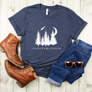 May include: A navy blue t-shirt with a white graphic of a crescent moon, shooting star, and pine trees. The text "Wander & Wonder" is printed below the graphic.