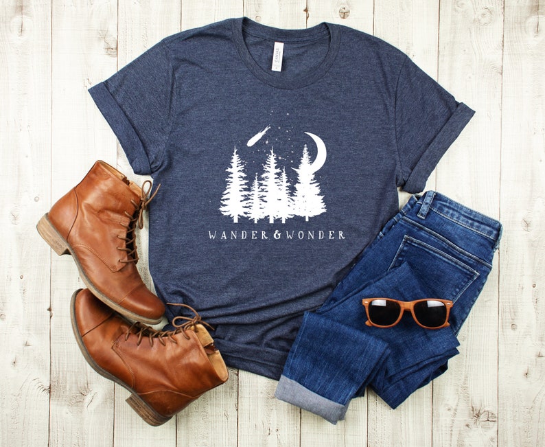 May include: A navy blue t-shirt with a white graphic of a crescent moon, shooting star, and pine trees. The text "Wander & Wonder" is printed below the graphic.