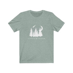 May include: A teal green t-shirt with a white graphic of a crescent moon, shooting star, and a group of pine trees. The text "WANDER & WONDER" is printed below the graphic.