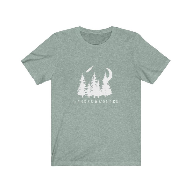 May include: A teal green t-shirt with a white graphic of a crescent moon, shooting star, and a group of pine trees. The text "WANDER & WONDER" is printed below the graphic.