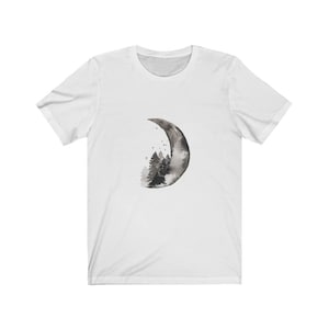 May include: White t-shirt with a black and white watercolor design of a crescent moon with a forest inside.