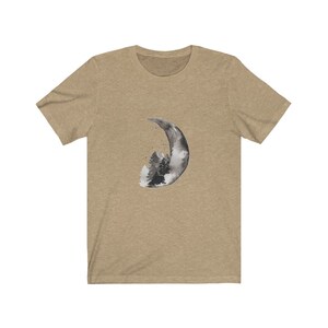 May include: A tan t-shirt with a black and white watercolor design of a crescent moon with a forest inside.