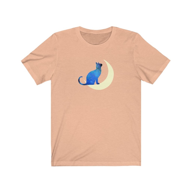 May include: A peach-colored t-shirt with a blue silhouette of a cat sitting on a crescent moon.