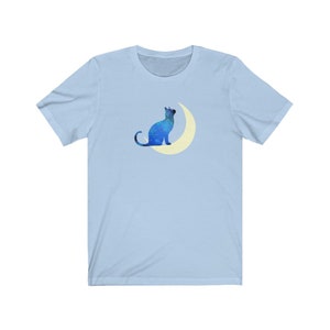 May include: A light blue t-shirt with a blue silhouette of a cat sitting on a crescent moon.