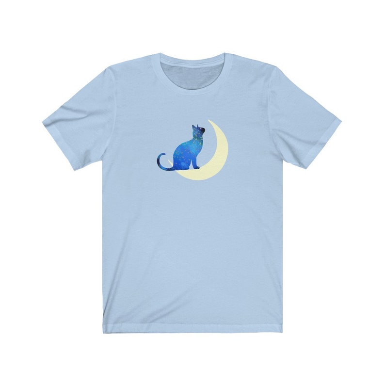 May include: A light blue t-shirt with a blue silhouette of a cat sitting on a crescent moon.