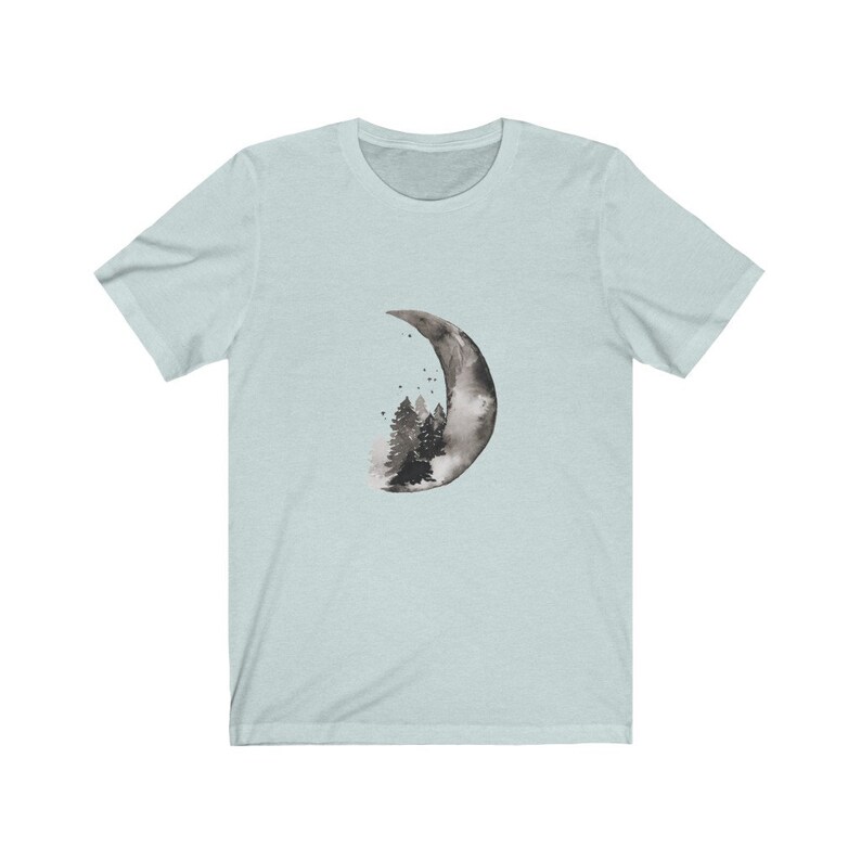 May include: A light blue t-shirt with a black and white watercolor design of a crescent moon with a forest inside.
