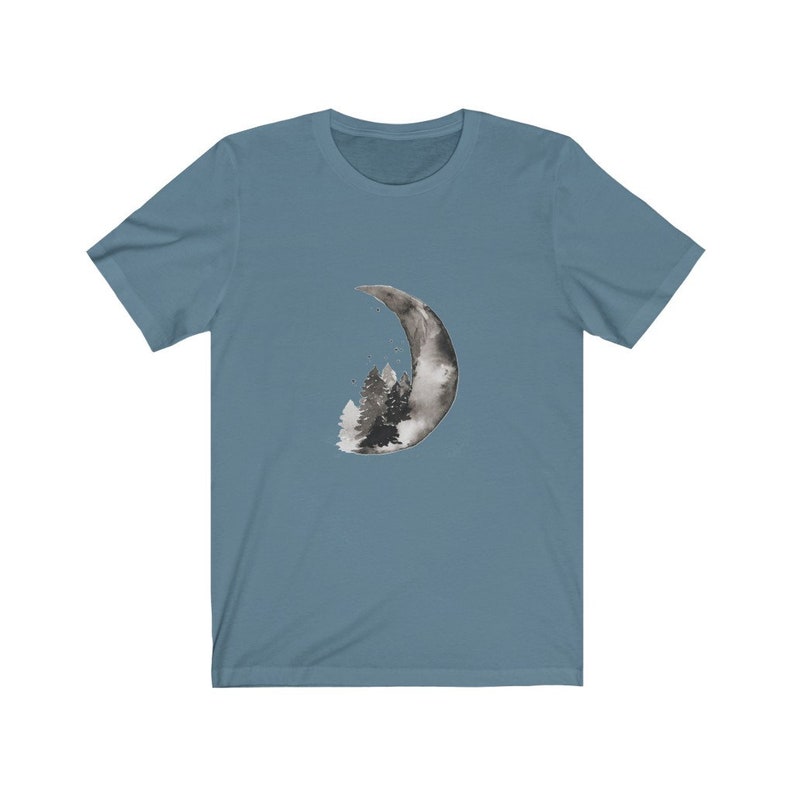 May include: A blue t-shirt with a black and white watercolor design of a crescent moon with a forest inside.
