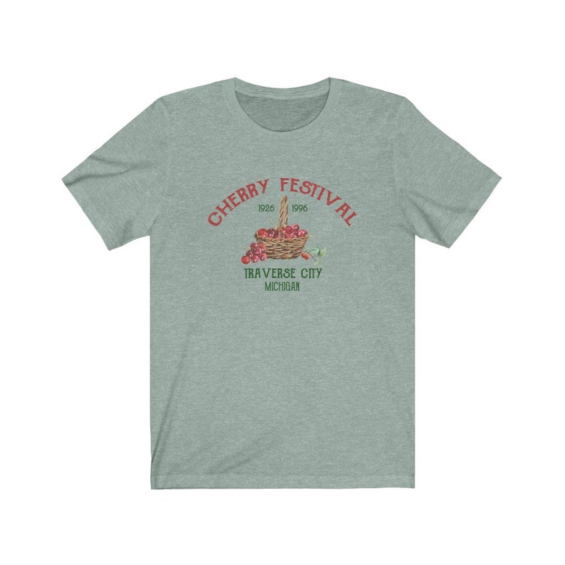 May include: A teal blue t-shirt with a red graphic of a basket of cherries. The graphic says "Cherry Festival 1926 1996 Traverse City Michigan".