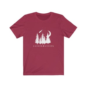 May include: A maroon t-shirt with a white graphic of a crescent moon, a shooting star, and a group of pine trees. The text "WANDER & WONDER" is printed below the graphic.
