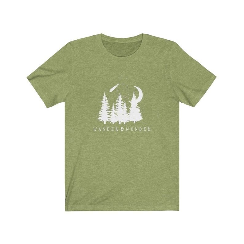 May include: A green short-sleeved t-shirt with a white graphic of a crescent moon, shooting star, and a group of pine trees. The text "WANDER & WONDER" is printed below the graphic.