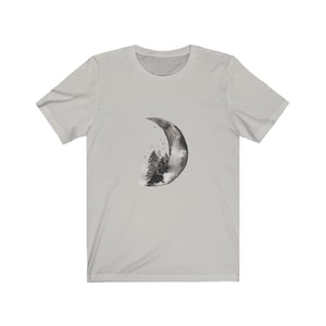 May include: A light gray t-shirt with a black and white watercolor design of a crescent moon with a forest inside.