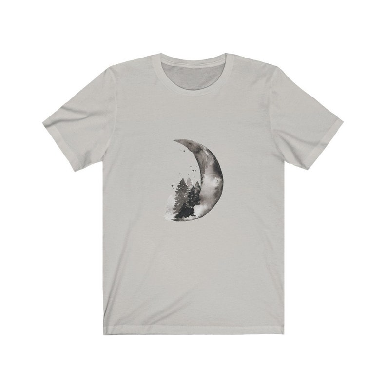 May include: A light gray t-shirt with a black and white watercolor design of a crescent moon with a forest inside.