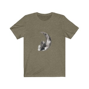 May include: A green t-shirt with a black and white watercolor design of a crescent moon with trees inside.