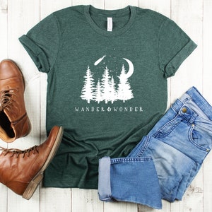 May include: A dark green t-shirt with a white graphic of trees, a crescent moon, and a shooting star. The text "Wander & Wonder" is printed below the graphic.