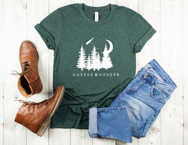 May include: A dark green t-shirt with a white graphic of trees, a crescent moon, and a shooting star. The text "Wander & Wonder" is printed below the graphic.