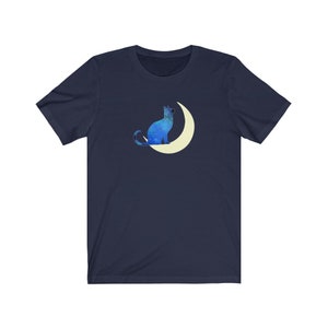 May include: A navy blue t-shirt with a blue cat sitting on a crescent moon. The cat and moon are both outlined in white.