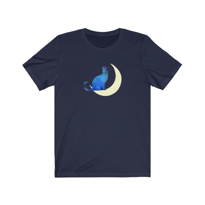 May include: A navy blue t-shirt with a blue cat sitting on a crescent moon. The cat and moon are both outlined in white.