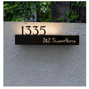 Op de afbeelding: Een rechthoekig huisnummerbord van zwart metaal met het verlichte nummer 1335 in een schreeflettertype en de tekst Z&Z Sweet Home in een schreefloos lettertype. Het bord straalt een warme gloed uit achter de cijfers voor een achtergrondverlichting.