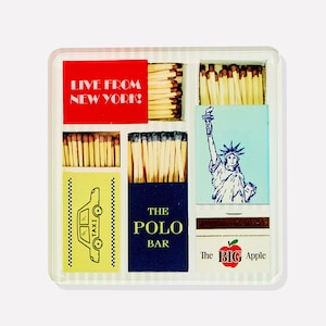 May include: A decorative matchbox set featuring various New York City-themed designs. The set includes matchboxes with text that reads "LIVE FROM NEW YORK!", "TAXI", "THE POLO BAR", and "The BIG Apple". The Statue of Liberty is also featured.