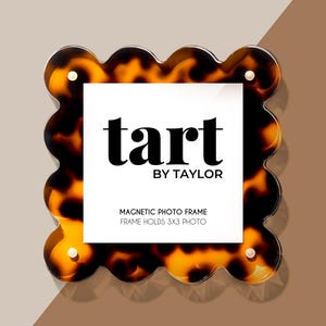 May include: A tortoiseshell magnetic photo frame with a scalloped edge. The frame holds a 3x3 photo and has the text "tart by taylor" and "Magnetic Photo Frame, Frame Holds 3x3 Photo" printed on it.