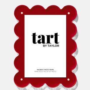 May include: A red, scalloped-edge magnetic photo frame with the text "tart BY TAYLOR" in black. The frame holds a 4x6 or 5x7 photo and has gold-colored accents. The frame is a decorative item.