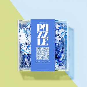 May include: A blue and white acrylic puzzle in a clear box. The box has a label that reads 