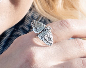 May include: A silver butterfly ring with intricate details. The ring is worn on the index finger of a person's hand.